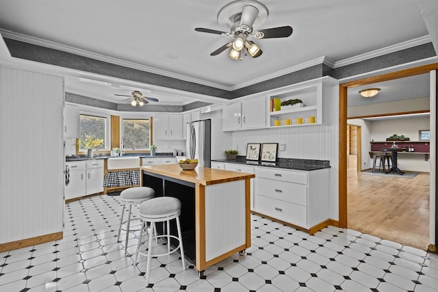 kitchen with white cabinetry, freestanding refrigerator, crown molding, butcher block counters, and light floors