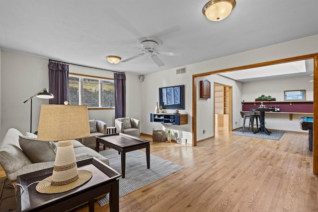 living area with baseboards, light wood-style floors, visible vents, and ceiling fan