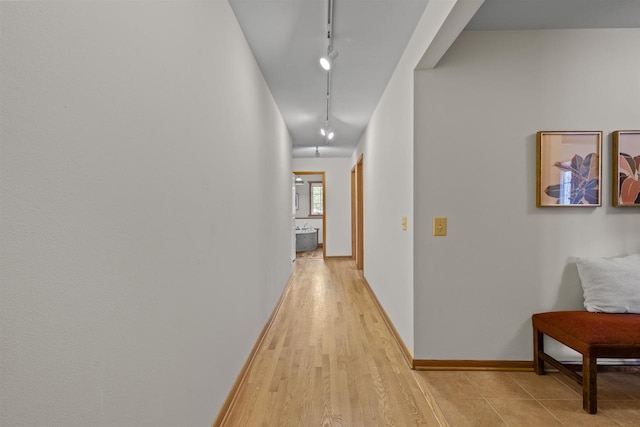 corridor featuring light wood-style flooring, rail lighting, and baseboards