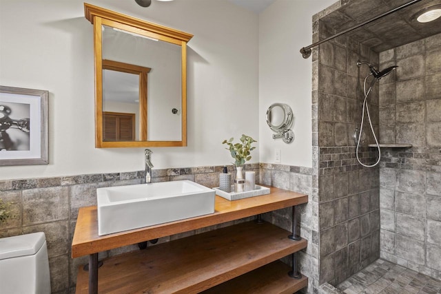 bathroom with a sink, tiled shower, toilet, and tile walls