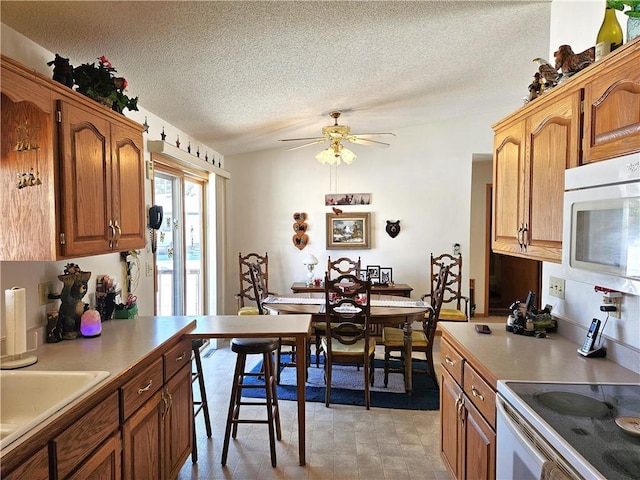 kitchen with brown cabinetry, light countertops, a textured ceiling, and white microwave