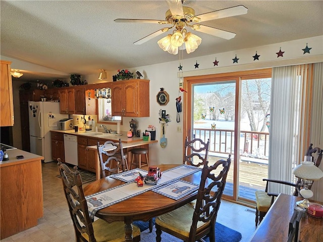 dining room with lofted ceiling, light floors, a textured ceiling, and a ceiling fan