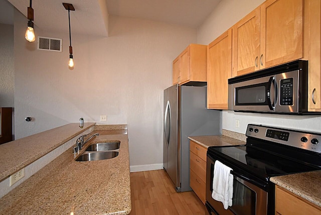 kitchen with decorative light fixtures, light wood finished floors, stainless steel appliances, visible vents, and a sink