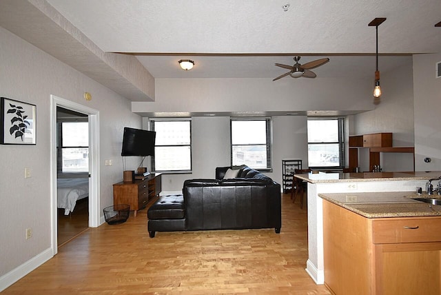 kitchen featuring hanging light fixtures, a sink, a ceiling fan, and light wood-style floors