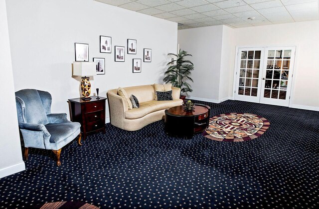 living room featuring baseboards, a drop ceiling, carpet flooring, and french doors