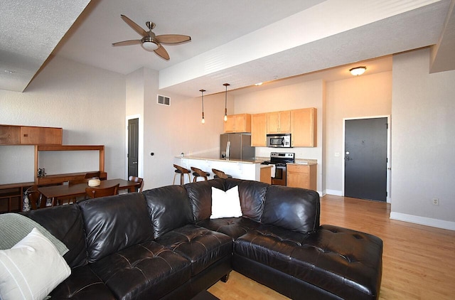 living area featuring visible vents, baseboards, light wood-style flooring, ceiling fan, and a high ceiling