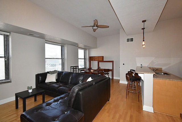 living room featuring baseboards, visible vents, ceiling fan, and light wood finished floors