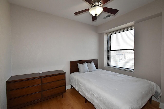 bedroom with a ceiling fan, visible vents, and wood finished floors