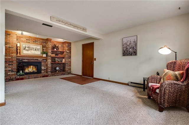 living area featuring a baseboard heating unit, a brick fireplace, carpet, and baseboards