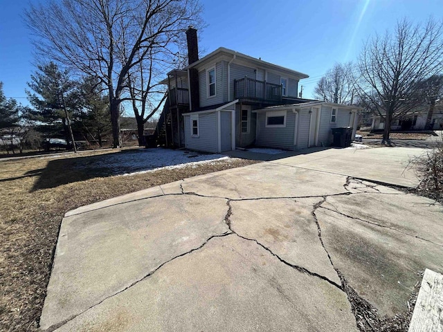 back of house with a chimney, driveway, and a balcony