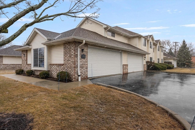 view of home's exterior with aphalt driveway, an attached garage, brick siding, a yard, and roof with shingles