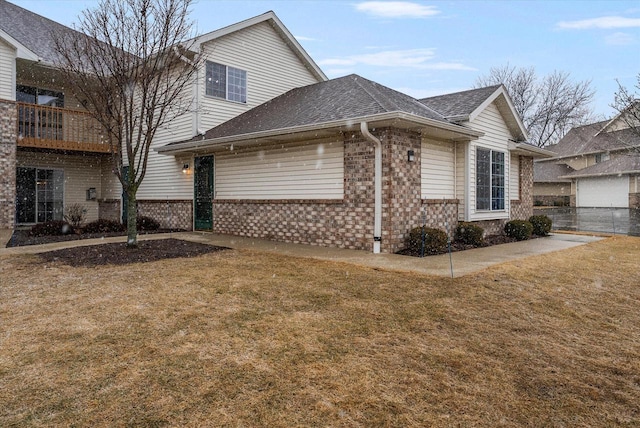 view of side of property with a yard, brick siding, a shingled roof, and fence