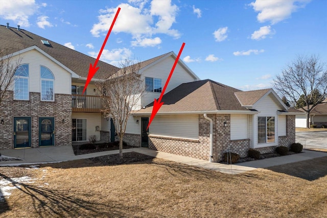 view of front of home with brick siding, roof with shingles, a front lawn, and a balcony