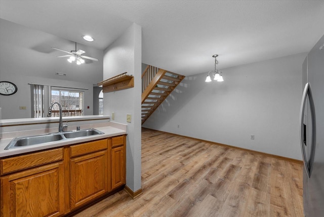 kitchen featuring brown cabinets, light countertops, freestanding refrigerator, a sink, and light wood-type flooring