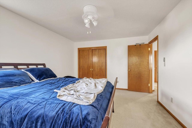 bedroom with baseboards, ceiling fan, a closet, and light colored carpet