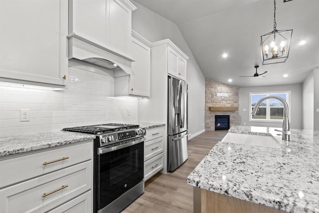 kitchen with a stone fireplace, a sink, open floor plan, appliances with stainless steel finishes, and tasteful backsplash