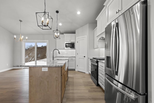 kitchen featuring a notable chandelier, stainless steel appliances, a sink, light wood finished floors, and tasteful backsplash