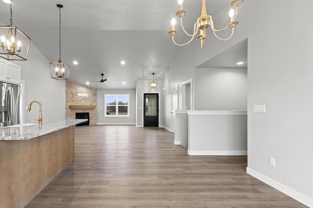 kitchen with a fireplace, light wood-style flooring, a sink, light stone countertops, and stainless steel fridge