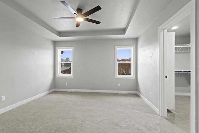 unfurnished bedroom with a tray ceiling, a walk in closet, multiple windows, and baseboards