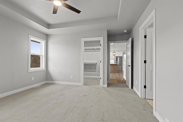 unfurnished bedroom with carpet, a raised ceiling, stainless steel fridge, and baseboards