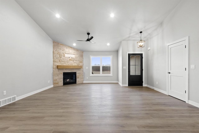 unfurnished living room featuring a fireplace, visible vents, wood finished floors, and ceiling fan with notable chandelier