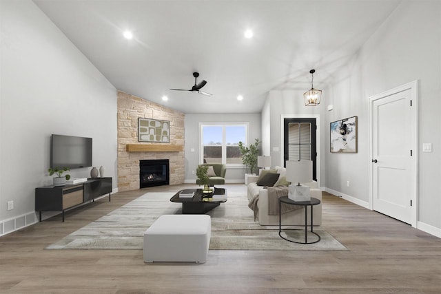 living room featuring high vaulted ceiling, ceiling fan with notable chandelier, a stone fireplace, and wood finished floors