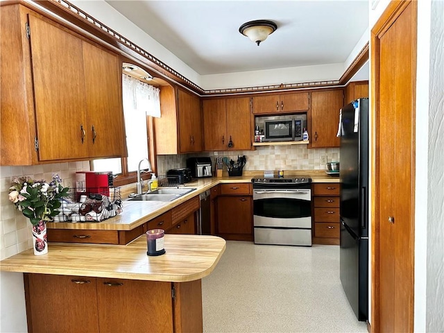 kitchen featuring a peninsula, a sink, backsplash, black appliances, and brown cabinetry