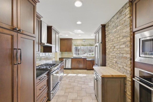 kitchen with built in appliances, stone finish flooring, wood counters, backsplash, and wall chimney exhaust hood