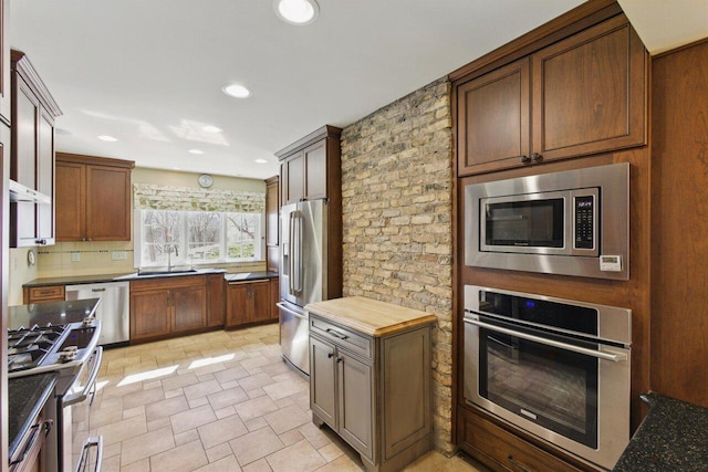 kitchen featuring recessed lighting, a sink, appliances with stainless steel finishes, backsplash, and stone finish flooring