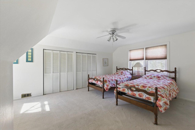 carpeted bedroom with lofted ceiling, a ceiling fan, visible vents, and two closets