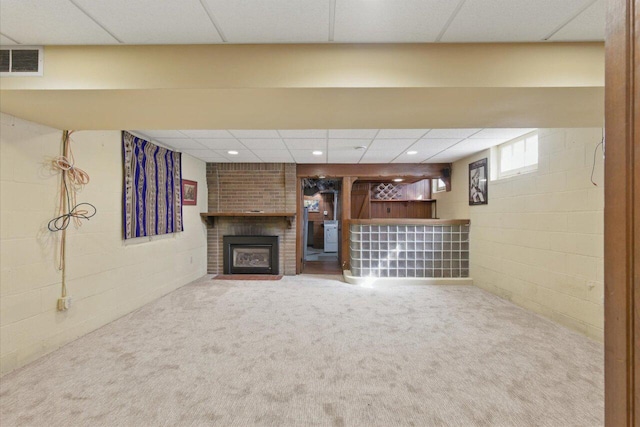 below grade area with concrete block wall, visible vents, a paneled ceiling, carpet floors, and a brick fireplace