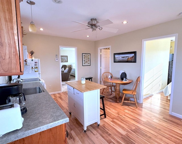 kitchen featuring baseboards, light wood-style floors, a kitchen bar, a sink, and recessed lighting