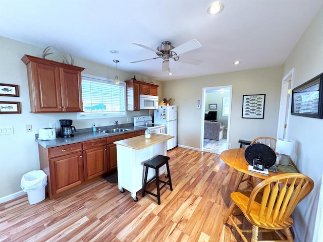 kitchen featuring recessed lighting, white appliances, a sink, light wood finished floors, and a kitchen bar