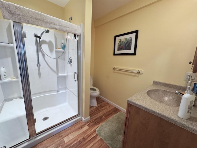 full bath featuring toilet, vanity, a shower stall, wood finished floors, and baseboards