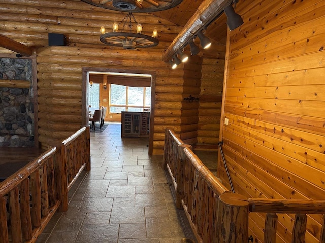 corridor with stone finish floor, a notable chandelier, an upstairs landing, and log walls