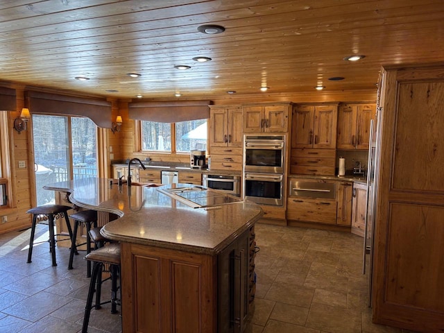 kitchen with stone finish floor, stainless steel appliances, a breakfast bar area, brown cabinetry, and wood ceiling