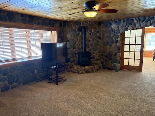 unfurnished living room featuring carpet, wood ceiling, ceiling fan, and a wood stove