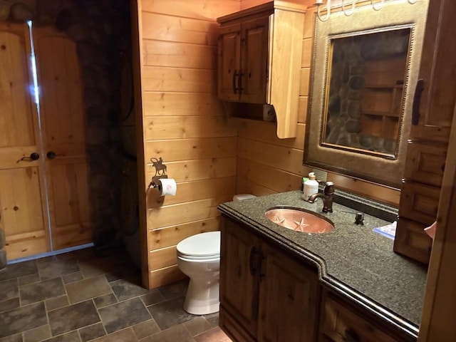 bathroom with wood walls, toilet, and vanity