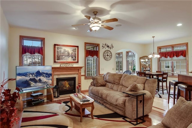 living area featuring ceiling fan with notable chandelier, a glass covered fireplace, and wood finished floors