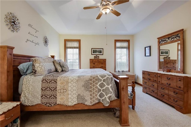 bedroom with ceiling fan, multiple windows, a tray ceiling, and light colored carpet