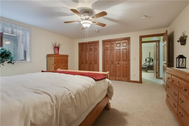 bedroom with multiple closets, light carpet, ceiling fan, and baseboards