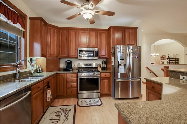 kitchen with arched walkways, stone countertops, a sink, appliances with stainless steel finishes, and light wood-type flooring