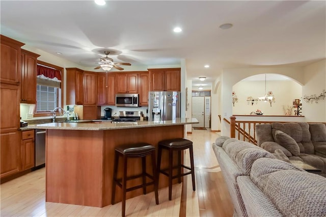 kitchen with appliances with stainless steel finishes, open floor plan, a kitchen breakfast bar, light stone countertops, and light wood-style floors