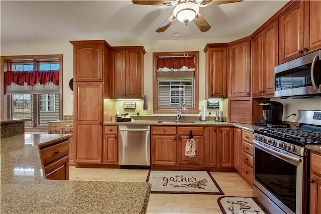 kitchen featuring appliances with stainless steel finishes, brown cabinetry, a sink, and light stone countertops