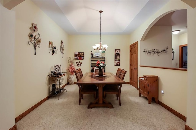 dining room featuring a chandelier, a tray ceiling, arched walkways, and baseboards