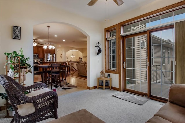 living room featuring arched walkways, ceiling fan with notable chandelier, carpet, and baseboards