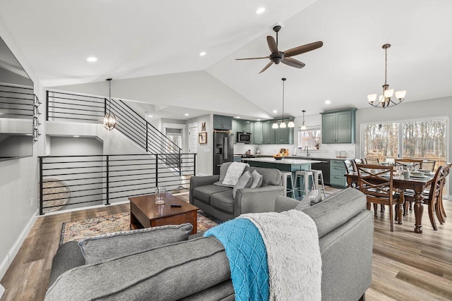 living room with stairs, recessed lighting, light wood-style floors, baseboards, and ceiling fan with notable chandelier