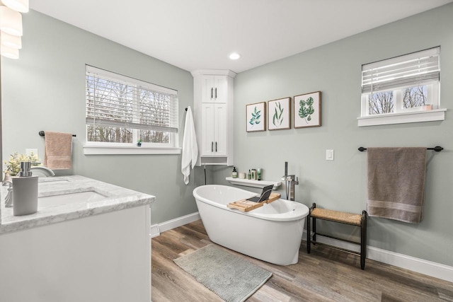 full bathroom featuring baseboards, wood finished floors, a freestanding bath, a sink, and recessed lighting