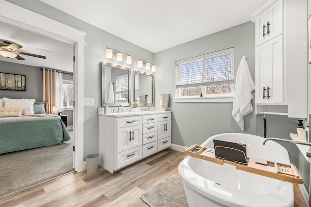 bathroom with double vanity, a freestanding bath, ensuite bath, wood finished floors, and baseboards