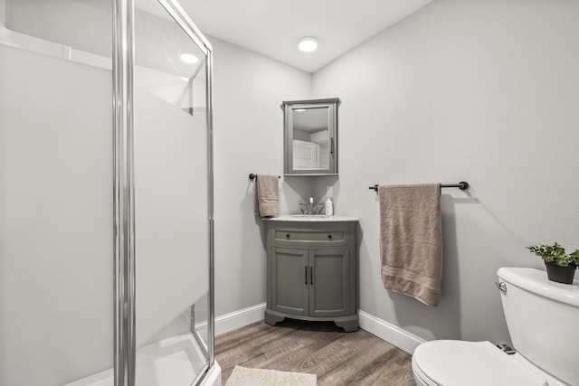 bathroom with baseboards, toilet, wood finished floors, vanity, and a shower stall